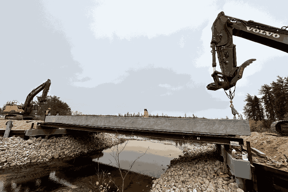 a construction site with a large excavator or bulldozer in the process of lifting a cement slab or bridge section